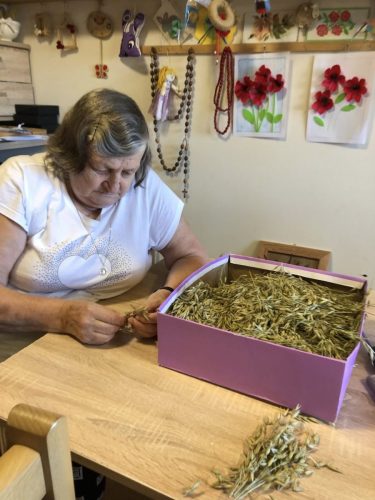11_08_2025_Przed świętem Matki Bożej Zielnej dopracowujemy i dekorujemy wieniec. Część osób dekorowała, a część Panów naprawiała ławę, a Panie kleiły motyle